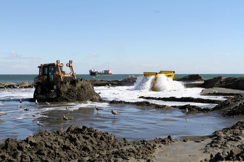 bulldozers spread the sand as it arrives on the beach