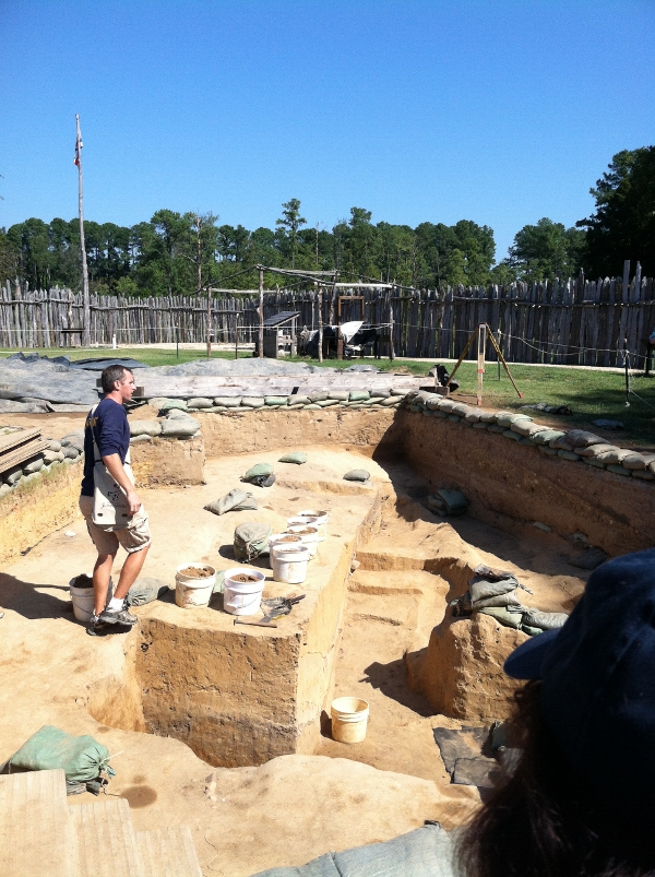 archeologists are excavating the original Jamestown fort, first built in 1607 and rebuilt after total destruction by fire in 1608 (with modern recreation of colonial palisade in background)